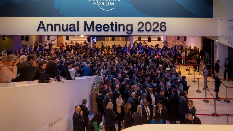 A high-angle view of delegates and media filling the entrance beneath the Annual Meeting 2026 signage during the World Economic Forum in Davos, Switzerland.