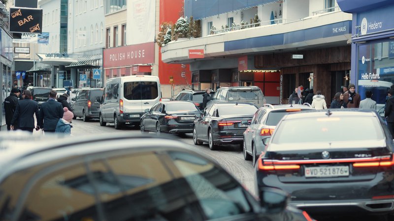 Traffic and pedestrians move between branded event venues on a busy central street during the World Economic Forum in Davos, Switzerland.