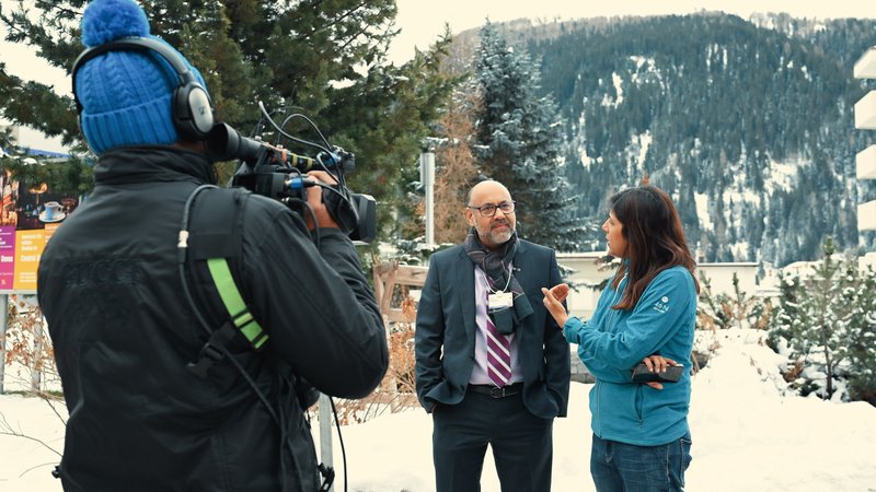 A camera operator films an outdoor interview against snow-covered mountains, documenting media activity during the World Economic Forum in Davos, Switzerland.