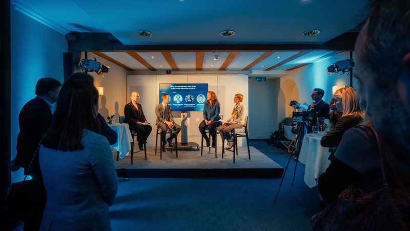 Four speakers take part in an intimate, blue-lit panel discussion as guests watch from both sides during the World Economic Forum in Davos, Switzerland.