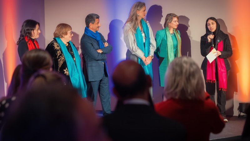 A woman addresses the audience with a microphone beside fellow participants on a warmly lit stage during the World Economic Forum in Davos, Switzerland.