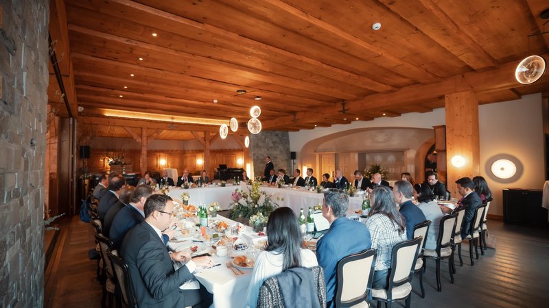 Delegates gather around an elegant table for a formal working lunch in a warm alpine interior during the World Economic Forum in Davos, Switzerland.