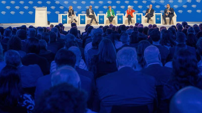 A full audience watches an international panel on a brightly lit blue stage during the World Economic Forum in Davos, Switzerland.